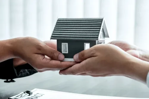 Duas pessoas a trocar uma casa miniatura com o logotipo Maxfinance 